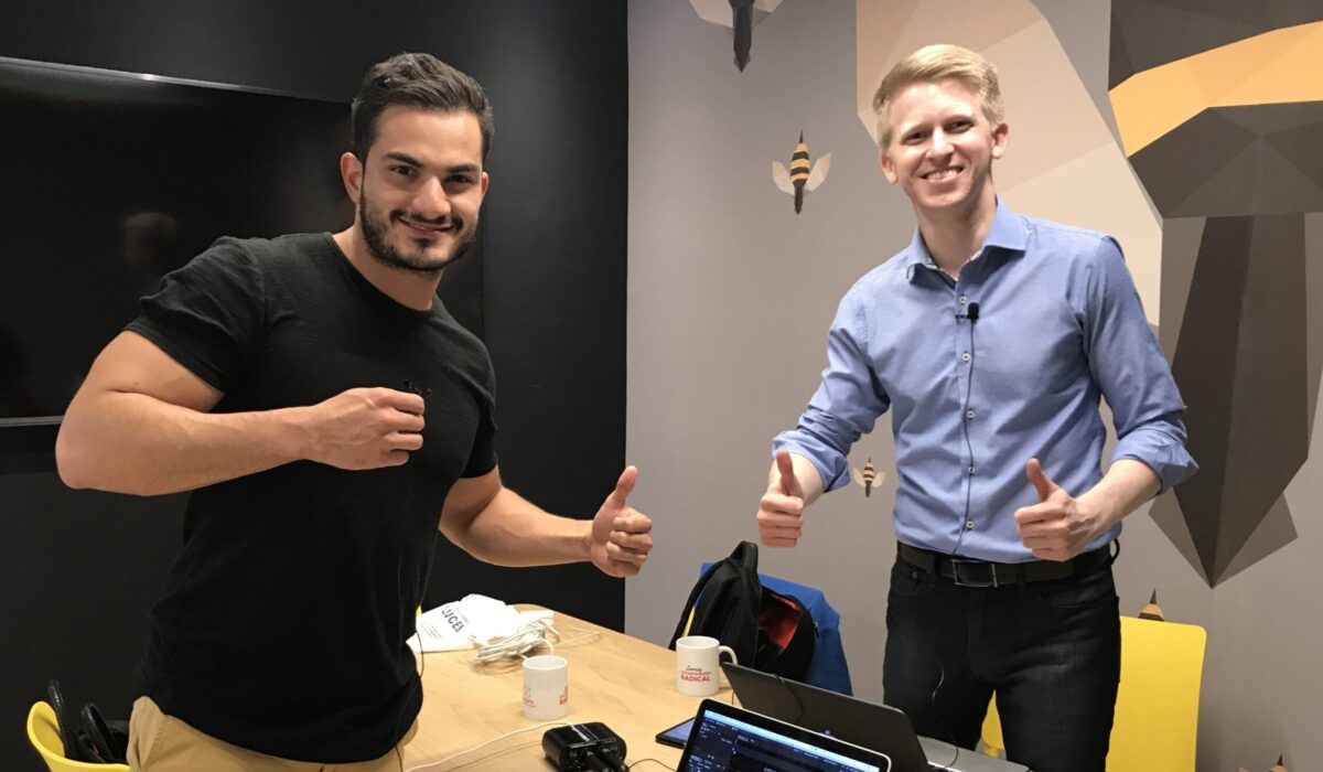 Two men smile at the camera with their thumbs up