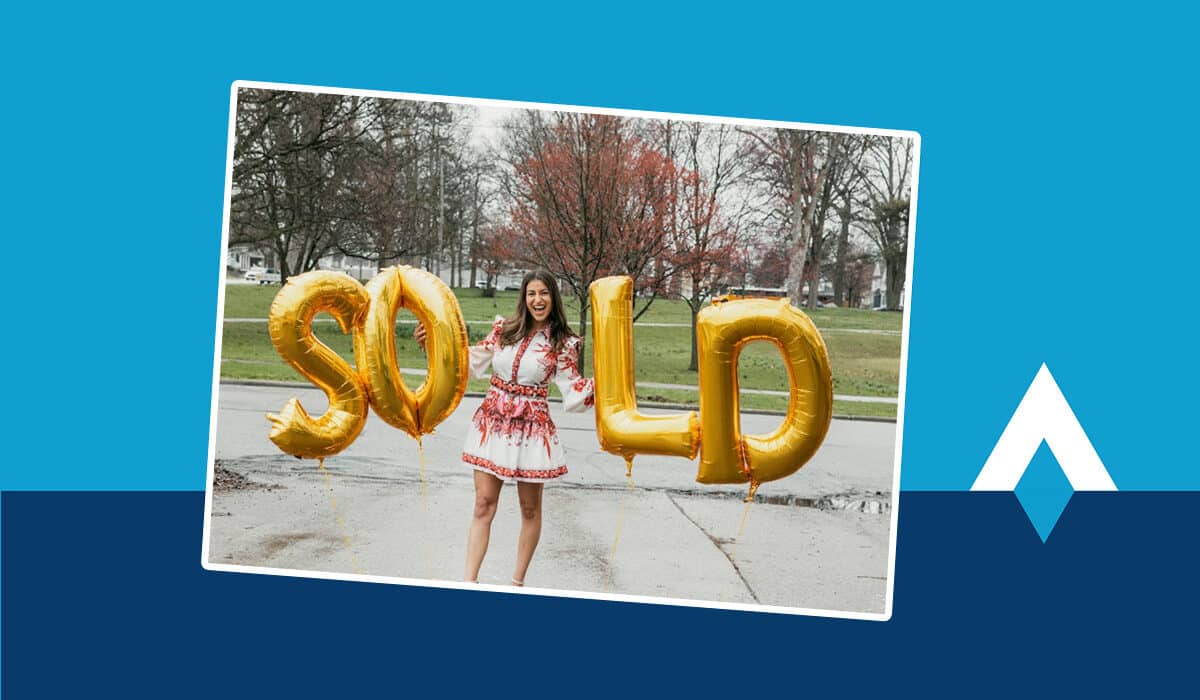 A photo sits on top of a blue background. In the photo, a woman stands smiling at the camera with gold letter balloons that spell out "SOLD."