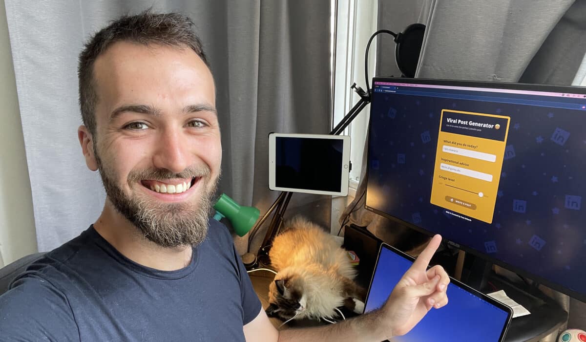 A man smiles at the camera while pointing to a computer screen in the background that shows the home screen for Viral Post Generator.