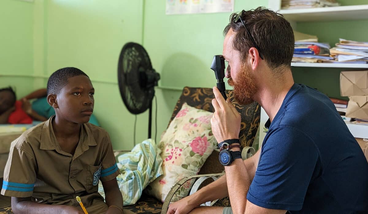 On the right is a man looking at a young patient's eye on the left with an ophthalmoscope.