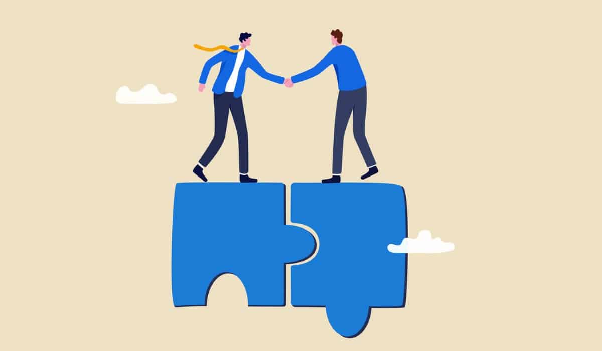 Two stylized figures stand on separate pieces of a puzzle that fit together, shaking hands. It symbolizes collaboration and the idea of two parts coming together to complete a whole.