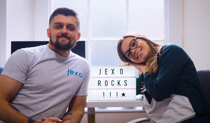 A man and a woman smiling at the camera with a lightbox sign that reads "JEXO ROCKS!!!" between them.